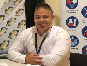 Ben Reed, BS, Altasciences' Executive Vice President of CDMO Operations, sits at a tall table in front of a conference booth.