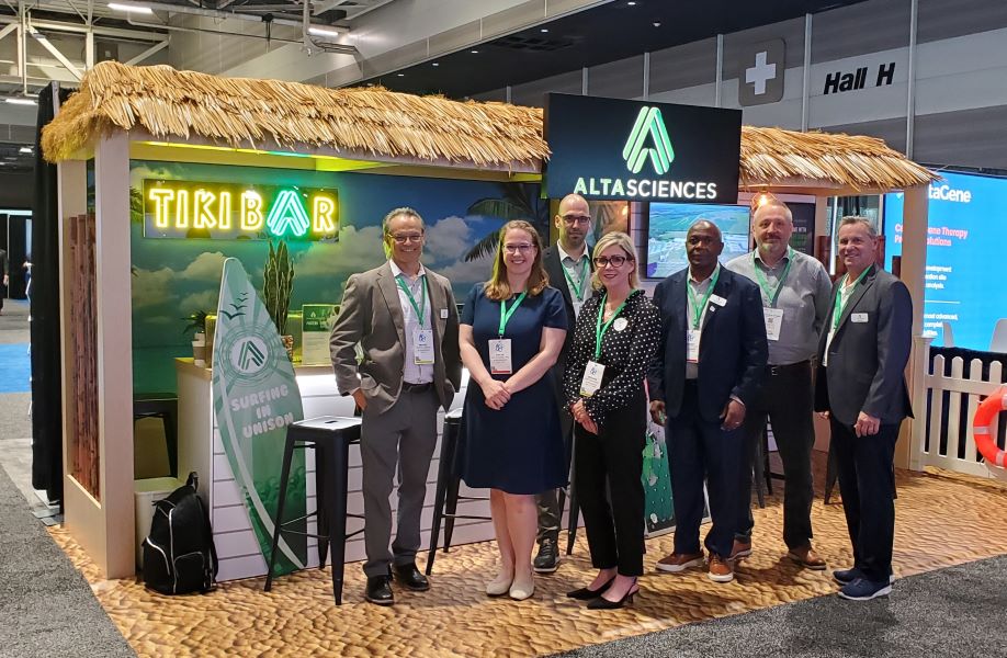 Employees from Altasciences smiling and posing in front of tiki bar-themed conference booth at ASGCT 2025.