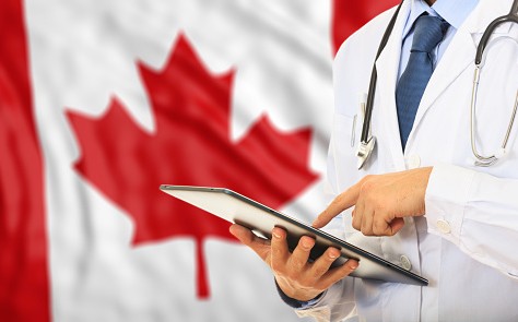 A Doctor checks a tablet in front of a Canadian flag